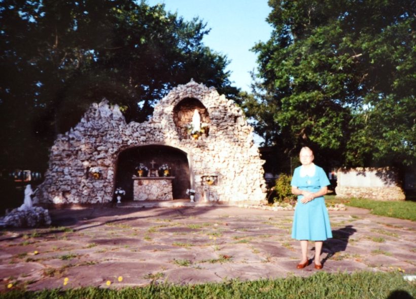 Antonia Kutra stojí u umělé jeskyně, která byla postavena ve Frydku po 2. světové válce. Vpravo je vidět pomník se jmény vojáků.