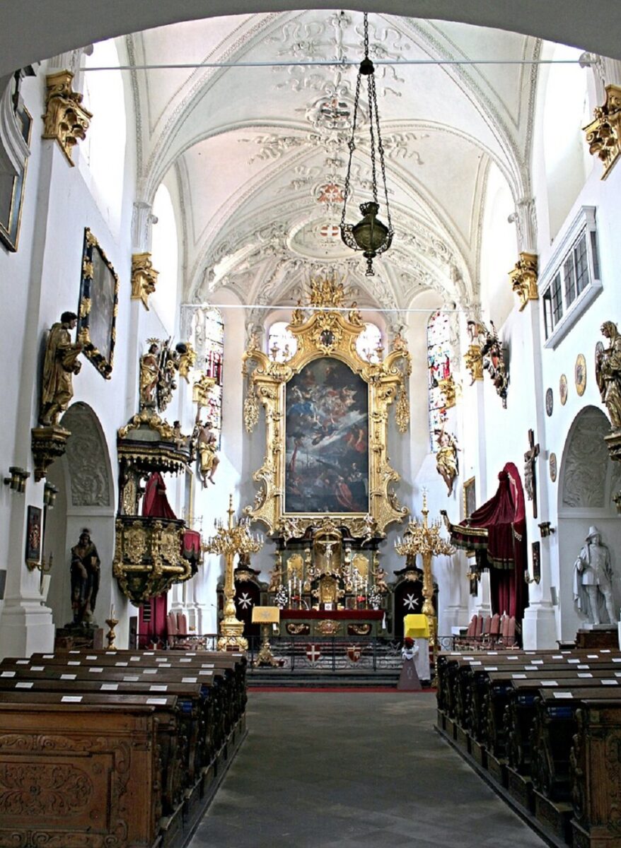 Hlavní oltář se Škrétovým obrazem, vlevo vyřezávaná kazatelna, vpravo socha R. Colloreda, v popředí barokní lavice.