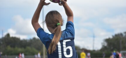 Mladá fotbalistka z Prahy 8 vhazuje míč zpět do hry. Symbol odhodlání, radosti z pohybu a práce klubů, které vedou dívky i chlapce ke sportu a zdravému životnímu stylu.