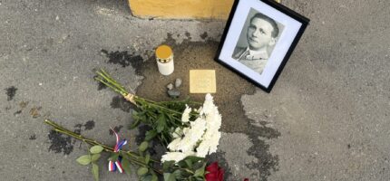 Květiny, zapálená svíčka a dobový portrét u jednoho z Kamenů zmizelých v Praze 2. Pietní místo připomíná tragický osud někdejšího obyvatele této městské části.
